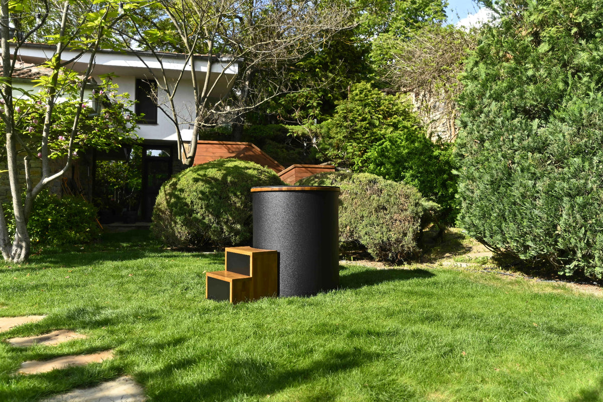 Temperd Barrel Pro cold plunge with wooden steps on a lawn in a landscaped garden